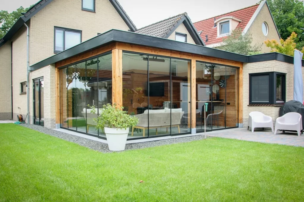 Moderne uitbouw met glazen wanden en houten staanders bij woning aan de Schouw